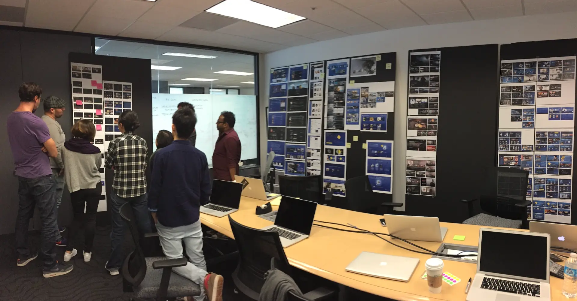 Cross-functional team gathered in a workshop room lined with interface boards